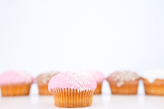 Many muffins with icing sugar lined up against a white background