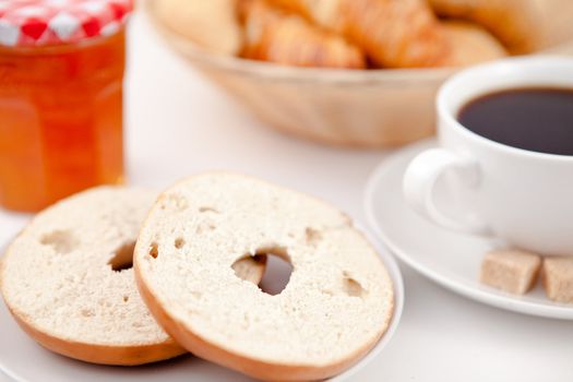 Doughnut cut in half and a cup of coffee on white plates with sugar and milk and a pot of jam against a white background