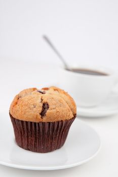 Muffin and a cup of coffee with a spoon on white plates against a white background