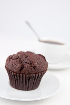 Chocolate muffin and a cup of coffee with a spoon on white plates against a white background