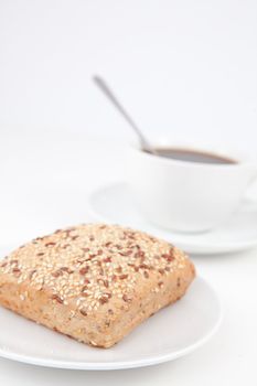 Bread bun and a cup of coffee with a spoon on white plates against a white background