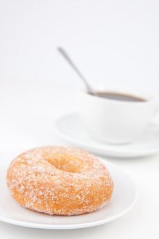 Doughnut with icing sugar and a cup of coffee with spoon on white plates against a white background