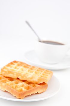 Waffles and a cup of coffee with a spoon on white plates against a white background