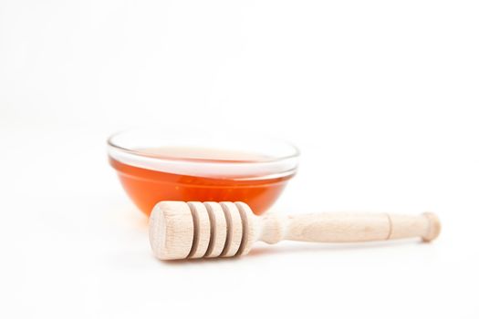 Honey bowl behind a honey dipper against a white background