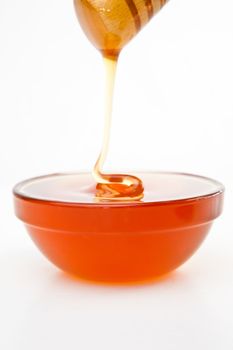 Honey trickle dropping in full honey bowl against a white background