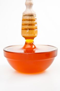 Honey trickle vertically dropping in full honey bowl against a white background