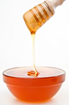 Honey trickle dropping in bowl against a white background