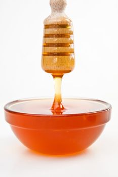 Thin honey trickle dropping in full honey bowl against a white background