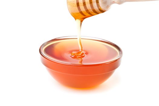 Honey trickle dropping in honey bowl against a white background