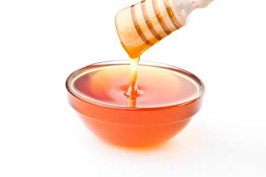 Honey dipper on top of a bowl against a white background