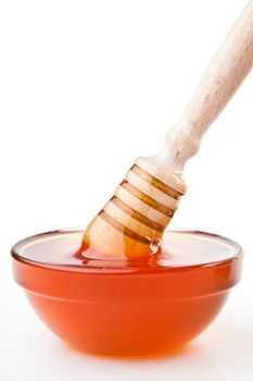 Honey dipper to the surface on  the honey bowl against a white background