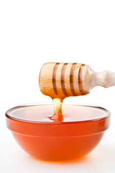 Honey dipper at horizontally  dropping a trickle of a honey against a white background