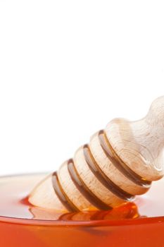 Close up of a honey dipper in a honey bowl against a white background