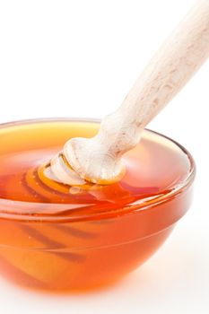 Close up of a honey bowl with a honey dipper against a white background