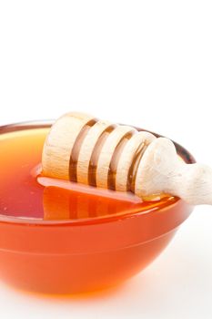 Honey dipper honrizontally on the edge of the bowl against a white background