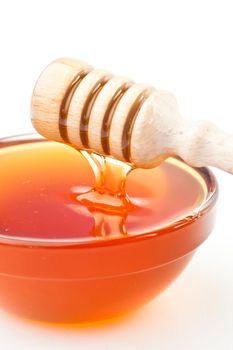 Honey sticky trickle dropping in a honey bowl against a white background