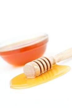 Honey dipper on the floor spilling honey in front of a honey bowl against a white background