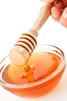 Honey dipper on the top of a bowl dropping honey against a white background