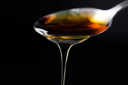 Honey trickle dropping of a full spoon against a black background