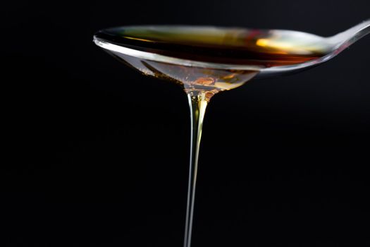 Honey trickle dropping of a spoon against a black background