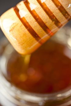 Honey dipper on top of a honey jar against a black background