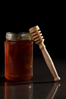 Honey jar and honey dipper against a black background