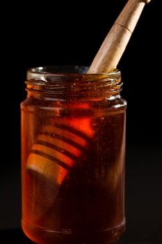 Honey dipper in a honey jar against a black background