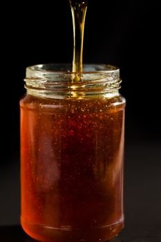 Honey trickle dropping in a honey jar against black background