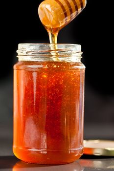 Honey sticky trickle dropping in a jar against a black background