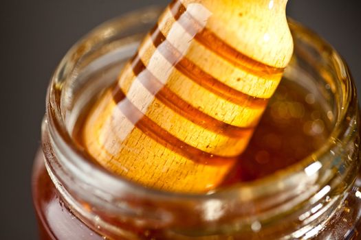Honey dipper outgoing a jar against a black background