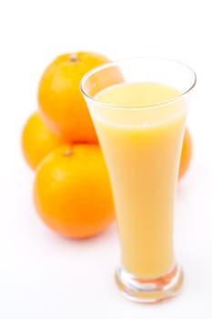 Oranges behind a glass of orange juice against white background
