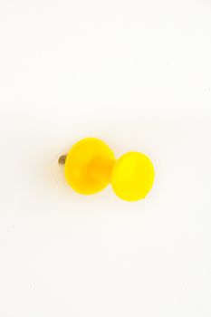Close up of a yellow pushpin pierced in the wall against a white background