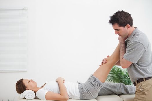 Chiropractor massaging a leg while placing it on his shoulder  in a room