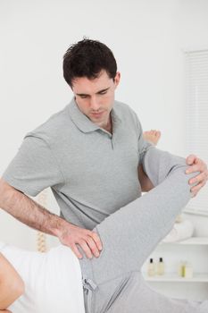 Physiotherapist standing behind a woman while stretching her leg in a room