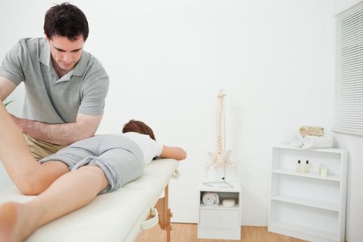 Serious brunette physiotherapist stretching the leg of a patient in a room