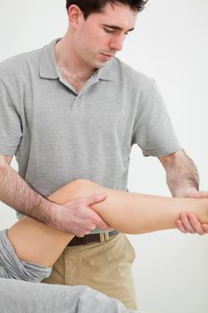 Serious osteopath examining a the leg of his patient in a room