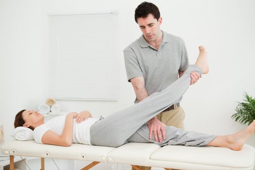 Brunette physiotherapist raising the leg of a patient in a room
