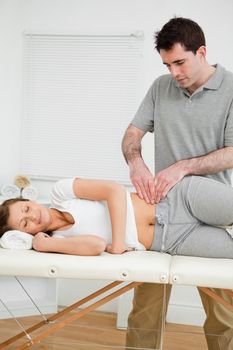 Serious physiotherapist checking the pelvis of a woman in a room