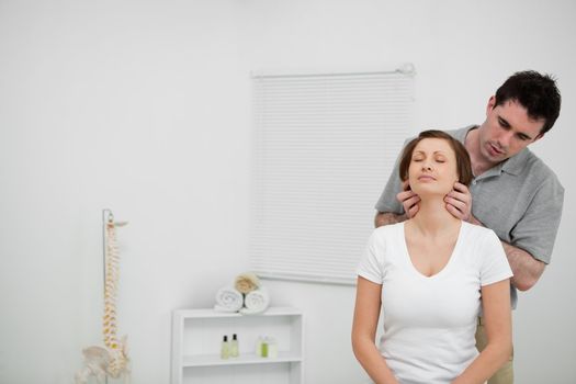 Serious osteopath palpating the neck of a woman in his office
