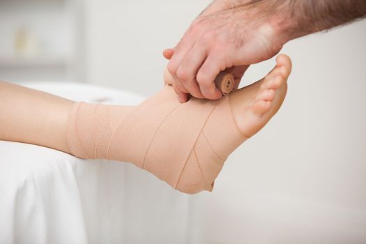 Practitioner bandaging an ankle in a medical room