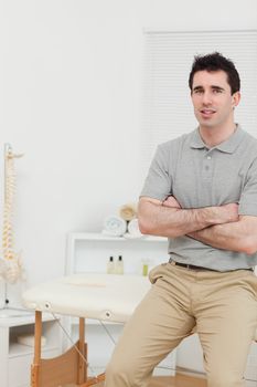 Peaceful osteopath sitting with arms crossed in his medical room