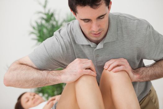 Serious doctor pressing on the knees of a patient in a room