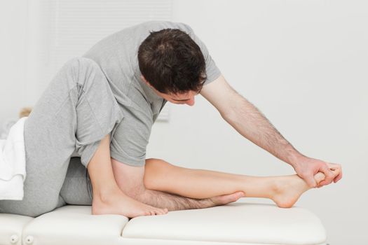 Brunette osteopath stretching a foot in a medical room