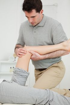 Serious physiotherapist looking at the knee of a patient in a room