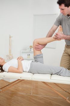Serious osteopath bending the leg of a woman in a room