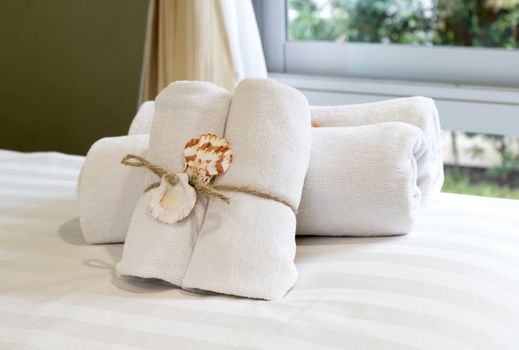 Closeup of soft white towels, rolled  folded and tied with rope and shell on bed.