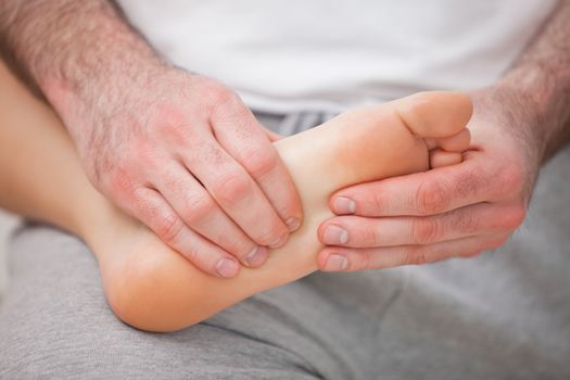 Podiatrist massaging the foot of a woman while holding it on his thigh indoors