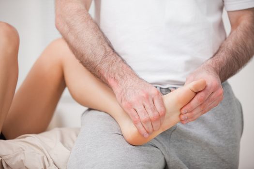 Reflexologist manipulating the foot of his patient while holding it on his thigh indoors