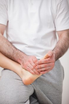 Podiatrist manipulating the foot of a woman while holding it on his thigh indoors