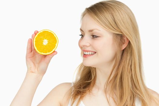 Joyful woman presenting an orange while looking at it against white background
